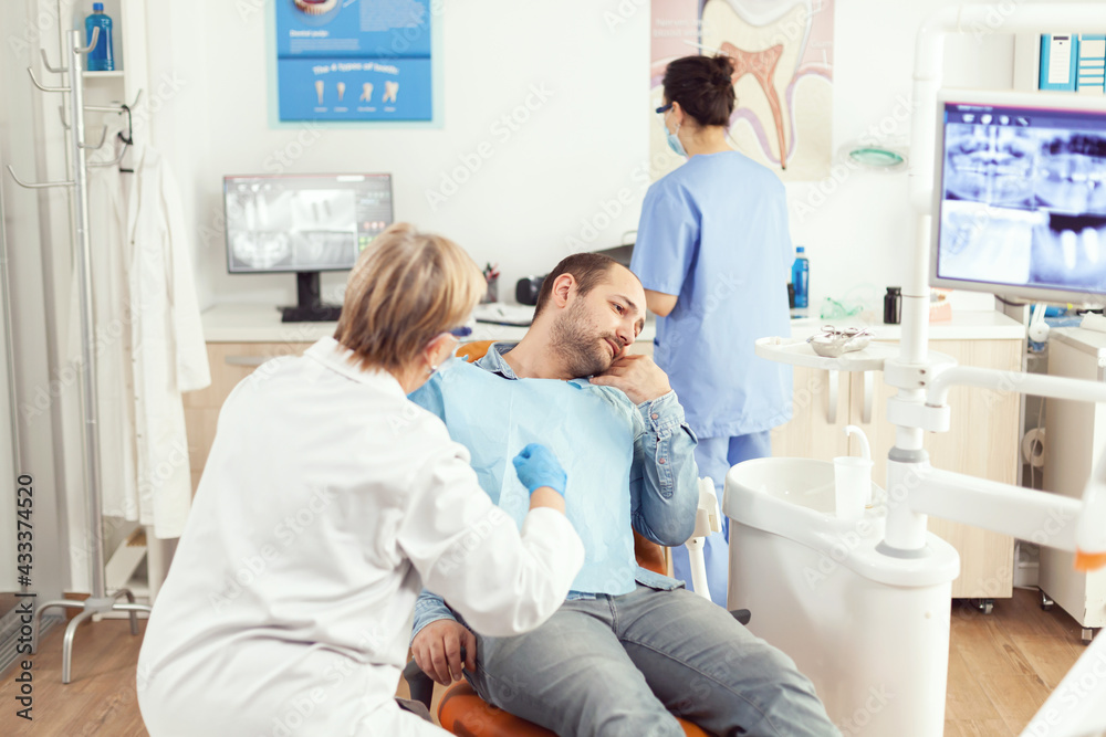 Obraz premium Stomatologist senior woman examining patient tooth pain during stomatology consultation. Sick man sitting on dental chair preparing for dentistry surgery waiting for toothache treatment