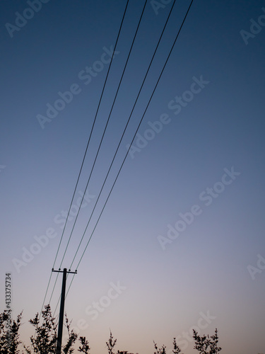 In summer, on the outskirts of the evening, the sky becomes dim, and telephone poles and wires stand by the roadside.