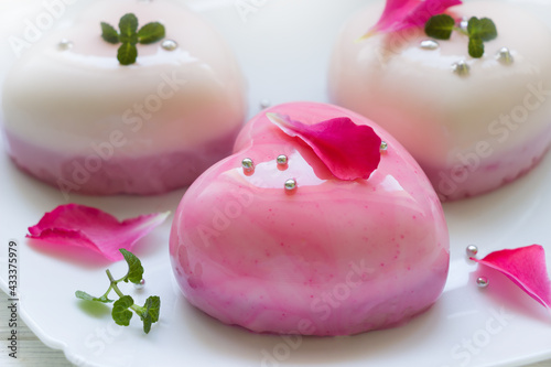 Modern  mousse cakes with pink  and white mirror glaze in the shape of a heart decorated with rose petals and mint leaves. Valentine's day background.Wedding cake