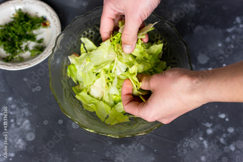 The man tears the leaves with his hands into a salad. Salad preparation.