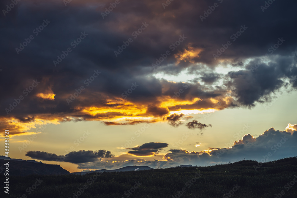 Beautiful mountain scenery with warm golden dawn light in cloudy sky. Scenic contrasting landscape with illuminating color in warm sunset sky. Gold illuminating sunlight. Contrast of warm sunrise sky.