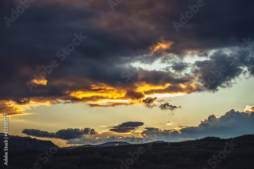 Beautiful mountain scenery with warm golden dawn light in cloudy sky. Scenic contrasting landscape with illuminating color in warm sunset sky. Gold illuminating sunlight. Contrast of warm sunrise sky. © Daniil