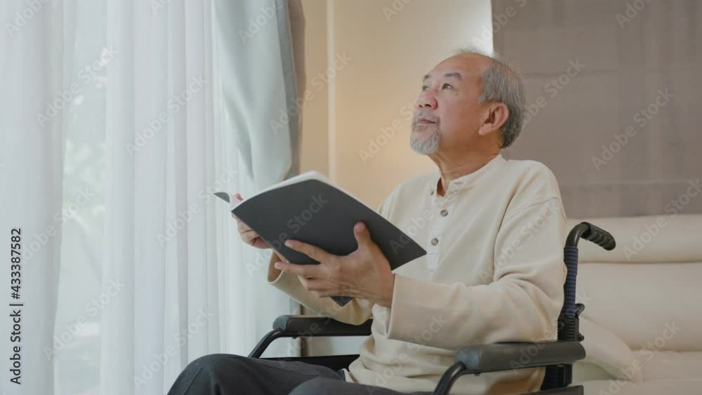Asian old man enjoy reading book sitting on wheelchair in nursing home Asian old man enjoy reading book sitting on wheelchair in nursing home
