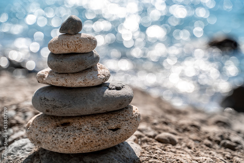 Tower of stones. Balanced pebble pyramid on the beach on a sunny day. Blue sea on the background. Selective focus  bokeh. Zen stones on the sea beach  meditation  spa  harmony  tranquility  balance