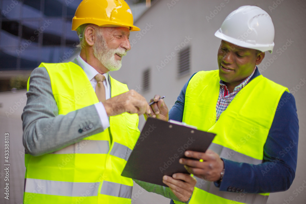 New business plan. Mature engineer discussing the structure of the building with architects colleague at construction site. New business plan. Mature engineer discussing the structure of the building with architects colleague at construction site.