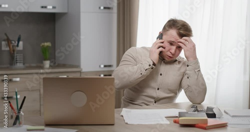 Man working at home sitting at his desk talking on the phone unpleasant conversation upset holding his head feels depressed crisis photo