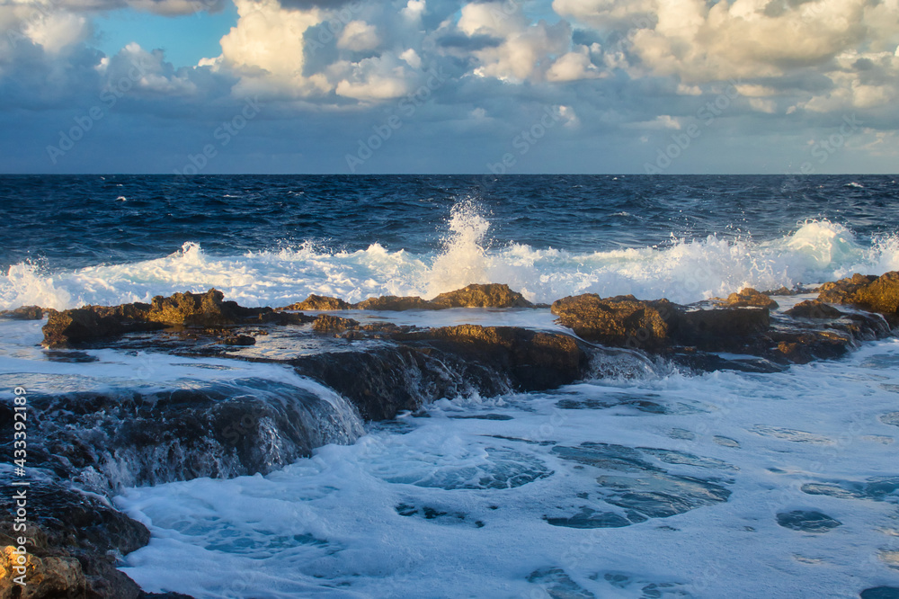 Light shining on the water as it splashes over rocks in the ocean at Qawra, Malta on a fall evening.