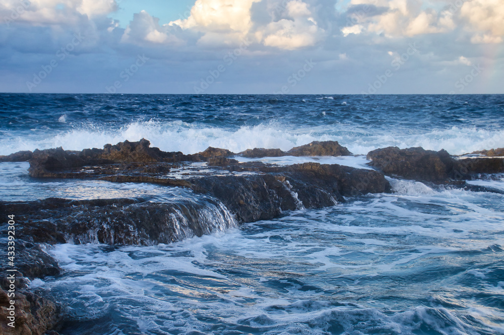 Water over rocks in the blue ocean at sunset in Qawra, Malta.