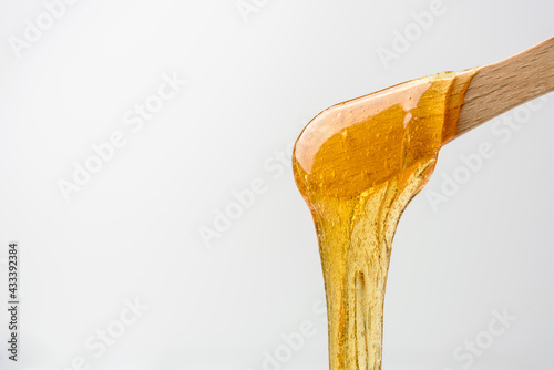 Canvas Print Liquid yellow sugar paste or wax for epilation on wooden stick or spatula closeu
