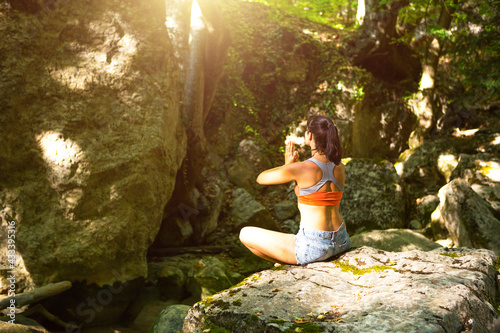 A woman sits in a lotus field on a large rock among the rocks in the open air and meditates, enjoys the unity with nature, listens to the silence and sounds of the forest. ecology