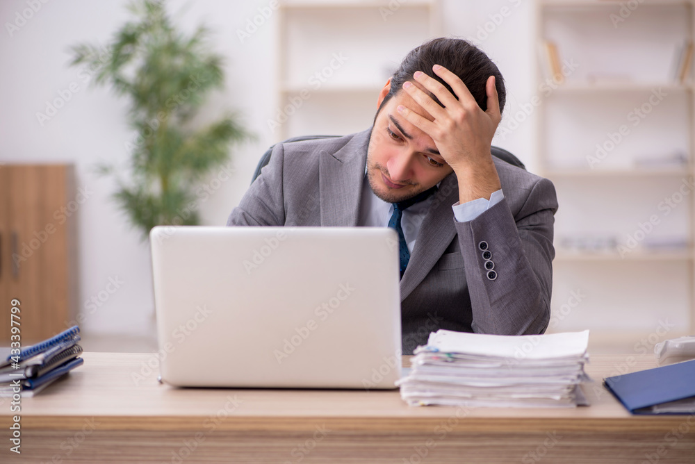Young male employee unhappy with excessive work in the office Young male employee unhappy with excessive work in the office