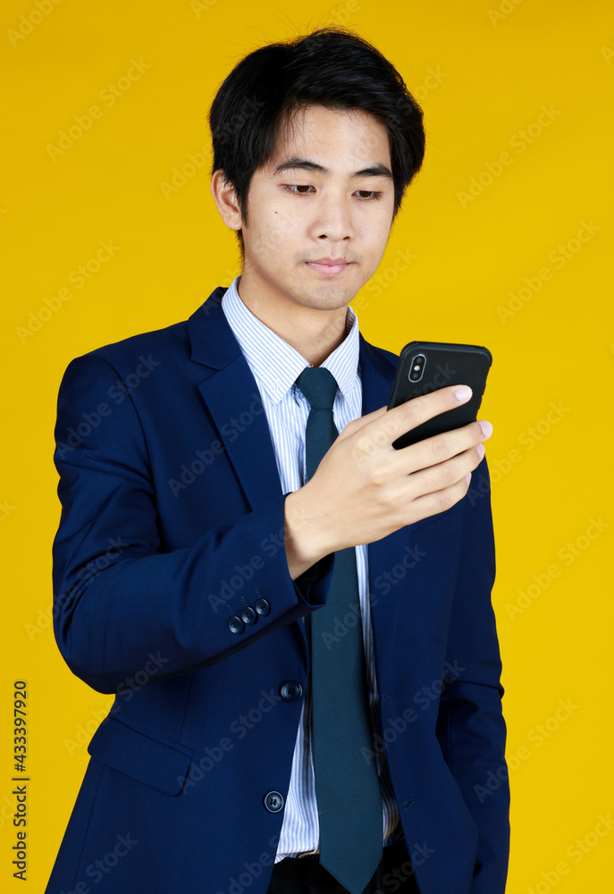 Handsome Businessman in formal blue suit. Standing look at mobile phone seems texting message. Yellow background gives modern feel. The space can fill with text. Handsome Businessman in formal blue suit. Standing look at mobile phone seems texting message. Yellow background gives modern feel. The space can fill with text.