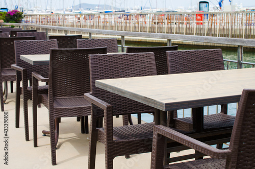 Wicker tables and chairs on the terrace of a cozy summer cafe overlooking the water.