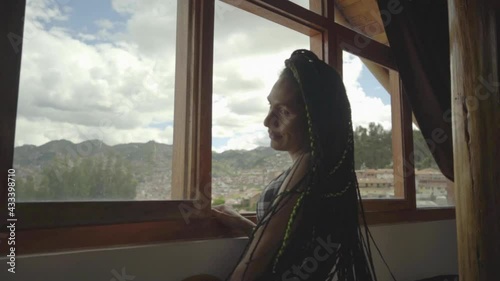 Mujer transgénero sonriendo y jugando con su cabello frente a la ventana de su habitación 