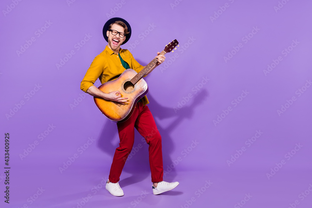 Full length body size view of attractive cheerful crazy guy playing guitar having fun isolated over bright violet purple color background Full length body size view of attractive cheerful crazy guy playing guitar having fun isolated over bright violet purple color background