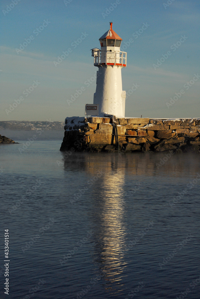 Skansen Light House, Trondheim, Norway. Standing on a mole reflected in the sea.