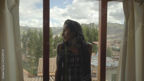 Mujer transgénero con trenzas observa el paisaje a través de su ventana 