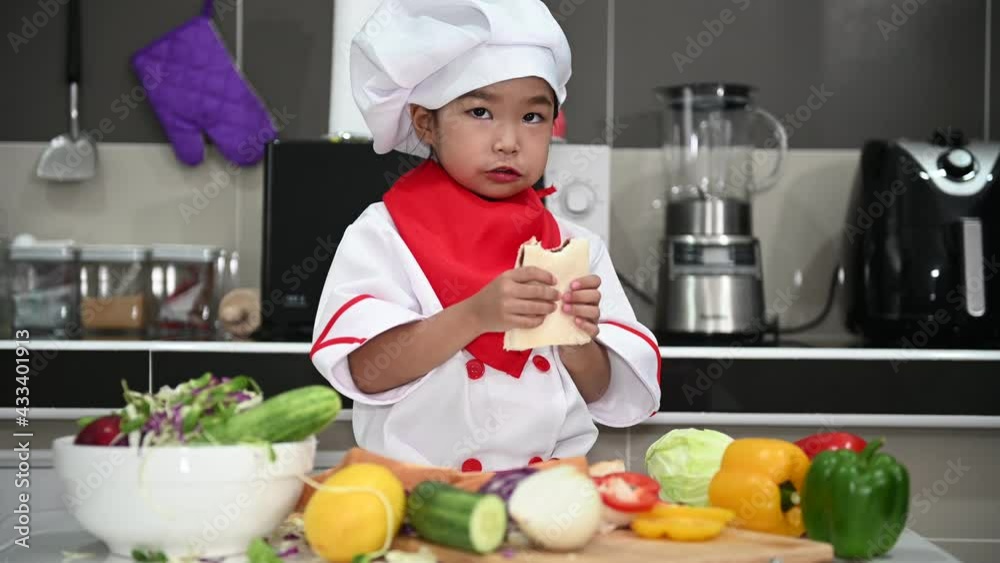 Cute asian girl wear chef uniform with a lot of vegatable on the table in the kitchen room,Make food for eat dinner,Funny time for kids Cute asian girl wear chef uniform with a lot of vegatable on the table in the kitchen room,Make food for eat dinner,Funny time for kids