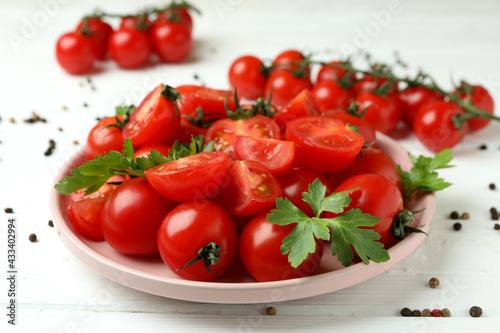 Plate with cherry tomato on white wooden background