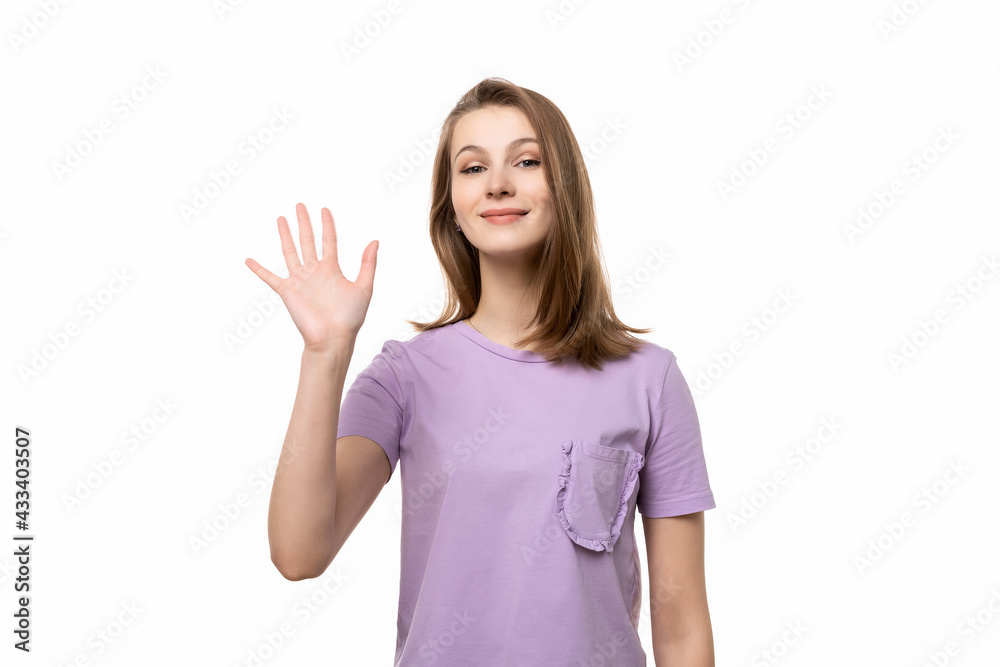 Friendly girl saying hello, smiling joyfully and friendly, waving her hand, showing five fingers Friendly girl saying hello, smiling joyfully and friendly, waving her hand, showing five fingers
