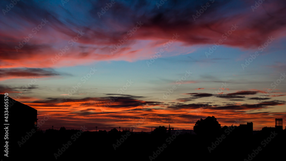 Sun rise with a black silhouette of some buildings and a very beautiful colored cloudy sky blue and orange