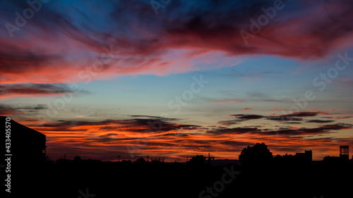 Sun rise with a black silhouette of some buildings and a very beautiful colored cloudy sky blue and orange © YomaOfficial