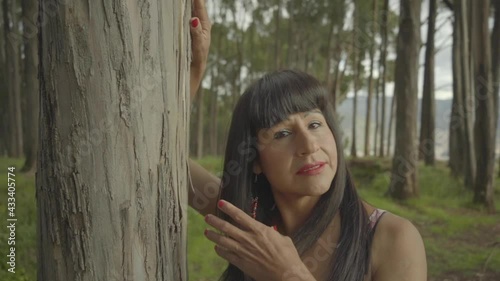 Mujer transgénero posando apoyada de un árbol en el bosque 