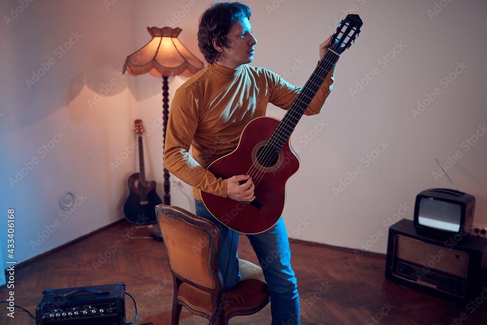 Obraz premium Male musician playing acoustic guitar on the amplifier in retro vintage room.