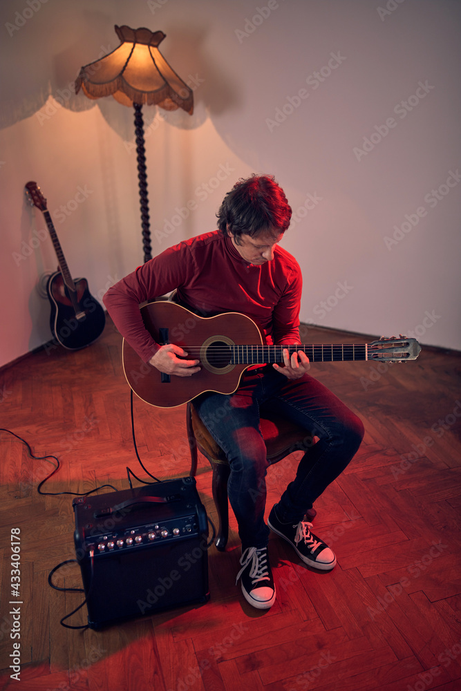 Obraz premium Male musician playing acoustic guitar on the amplifier in retro vintage room.
