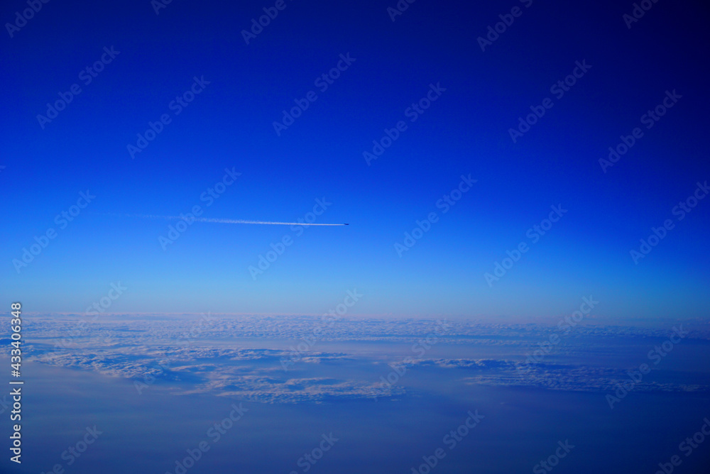 一面の雲海の上を長い飛行機雲を引きながら遠くを飛ぶジェット機