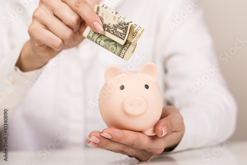 Woman putting dollar bancnote into piggy bank on light blue background, closeup. Space for text photo