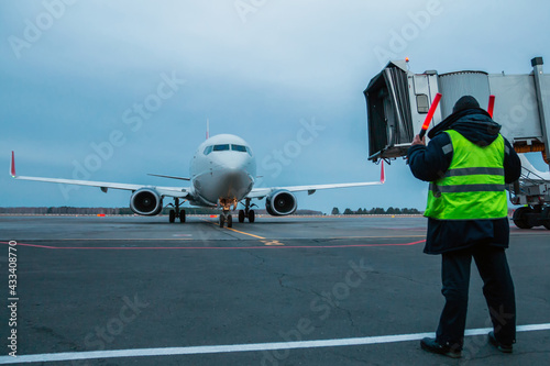 Airport marshaller meets passenger jet plane that taxiing to the parking lot at the airport apron photo