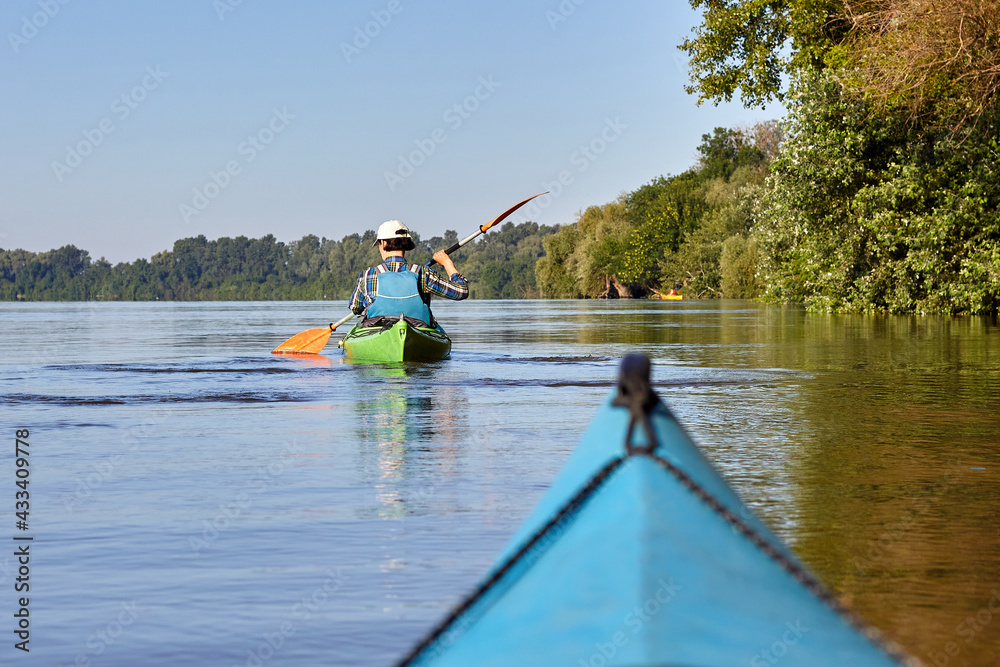 Woman kayaking in green kayak on the danube river at the morning. Back view