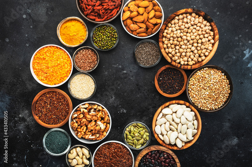 Selection of superfoods, legumes, cereals, nuts, seeds in bowls on black background. Superfood as chia, spirulina, beans, goji berries, quinoa, turmeric and other. Copy space, top view