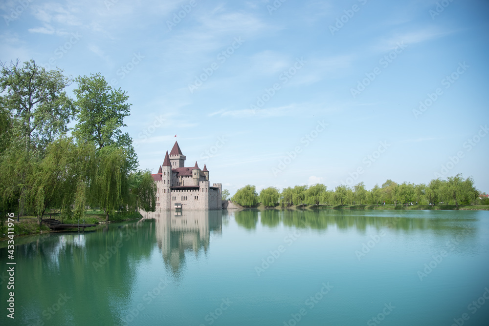 
Kabardino-Balkarian Republic, Russia, Chateau Erken, 05/01/2021 Castle on the water, bright blue water and sky. Reflection of a modern castle in the water. Tower. Willows on the shore.