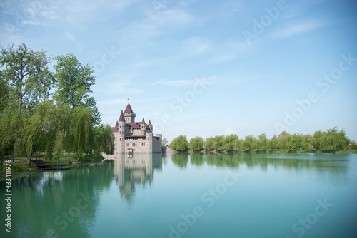 Kabardino-Balkarian Republic, Russia, Chateau Erken, 05/01/2021 Castle on the water, bright blue water and sky. Reflection of a modern castle in the water. Tower. Willows on the shore.