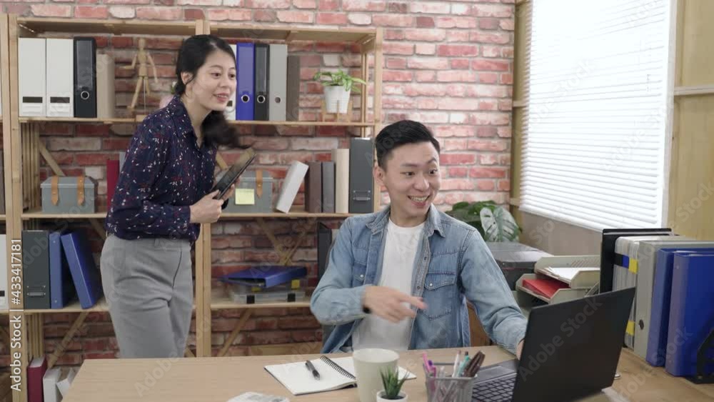 asian man using and pointing at computer screen is cheering for business success with his colleague by lifting clenched fist in an open loft office. asian man using and pointing at computer screen is cheering for business success with his colleague by lifting clenched fist in an open loft office.