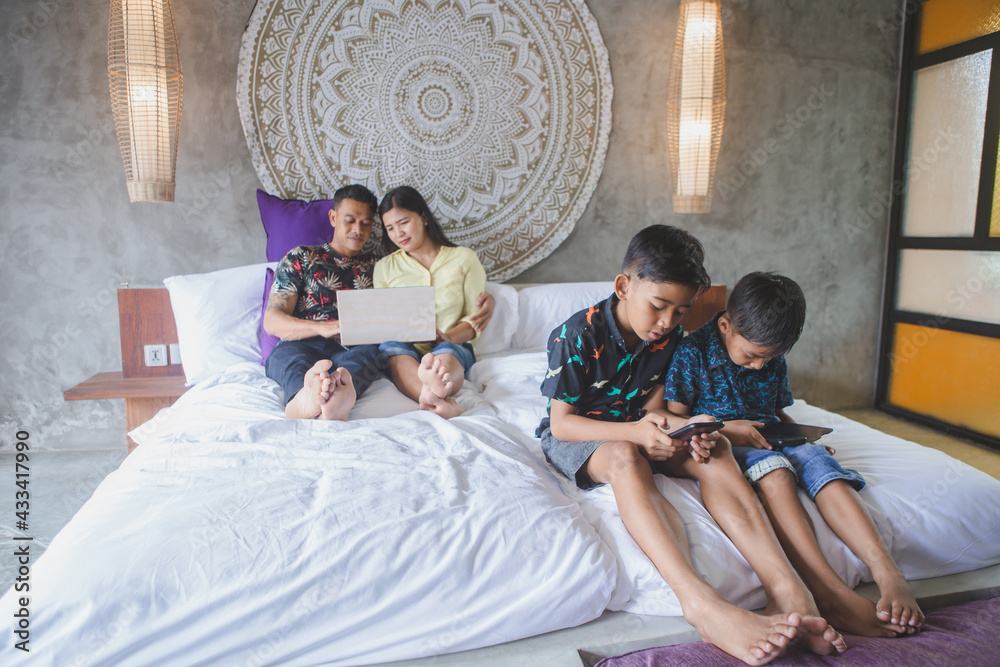 Indonesian or malasian family addicted to digital technology. Family at home using smartphones. Mom, dad and children obsessed with devices overusing social media, playing games or watching videos