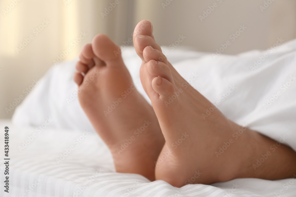 Person in bed with white linens at home, closeup on feet Person in bed with white linens at home, closeup on feet