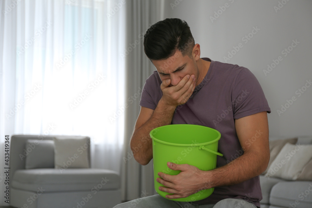 Man with bucket suffering from nausea at home, space for text. Food poisoning Man with bucket suffering from nausea at home, space for text. Food poisoning