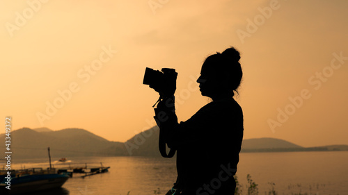 Photography Silhouette of young woman photographer, taking pictures of the landscape at suns