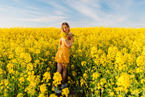 Portrait of attractive woman on blooming rapeseed field with sunset light. Yellow flowers and happy woman