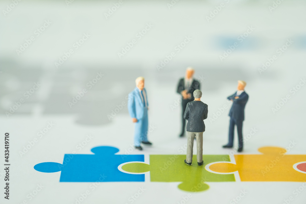 Miniature businessmen discuss financial result and standing on the white paper with jigsaw puzzles. Miniature businessmen discuss financial result and standing on the white paper with jigsaw puzzles.