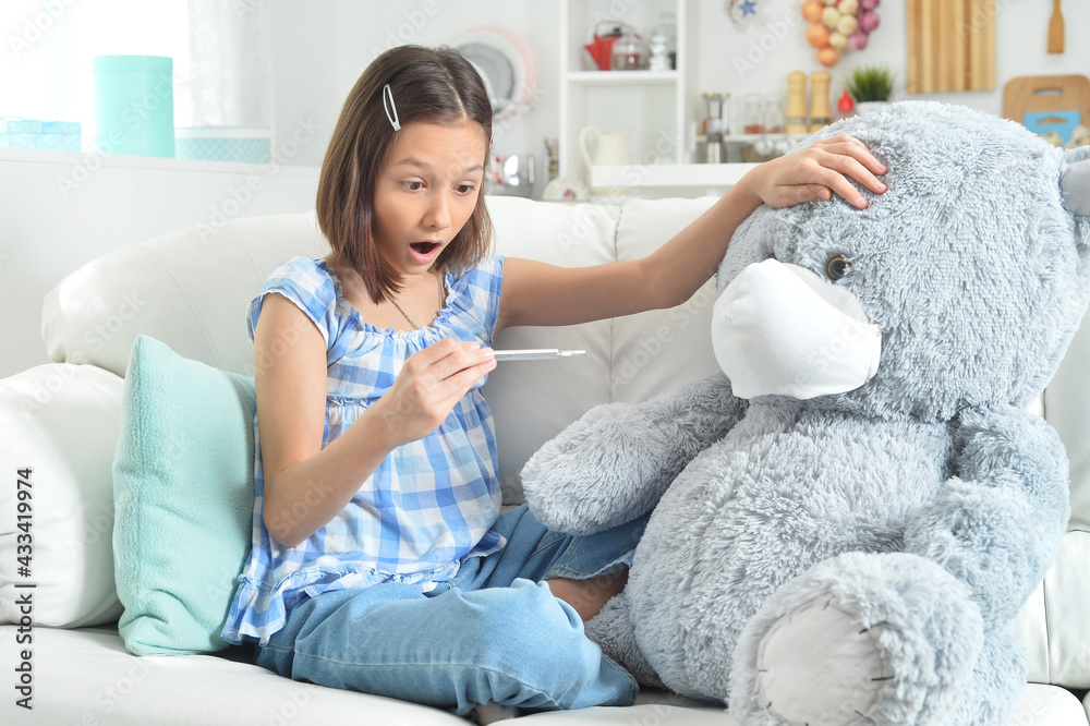 cute girl with thermometer playing with toy bear in facial mask cute girl with thermometer playing with toy bear in facial mask