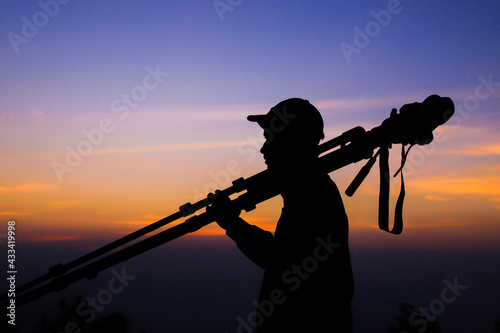 Silhouette of the photographer with tripod. Young Indian man taking photo with his camera during golden hour.