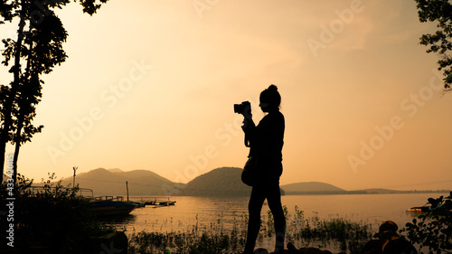 Canvas Print Silhouette of young woman photographer, taking pictures of the landscape at suns