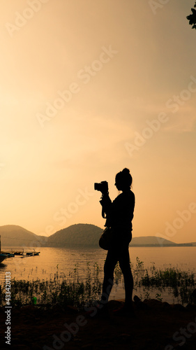 Canvas Print Silhouette of young woman photographer, taking pictures of the landscape at suns