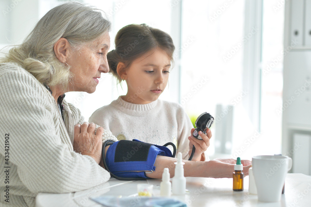 Cute girl and senior woman measuring blood pressure