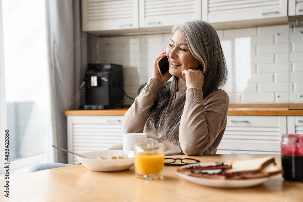 Mature smiling woman talking on cellphone while having breakfast Mature smiling woman talking on cellphone while having breakfast