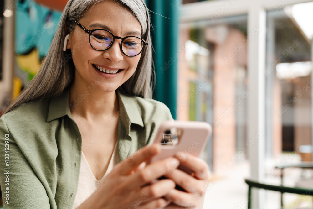 Mature smiling woman using earphone and mobile phone in cafe Mature smiling woman using earphone and mobile phone in cafe